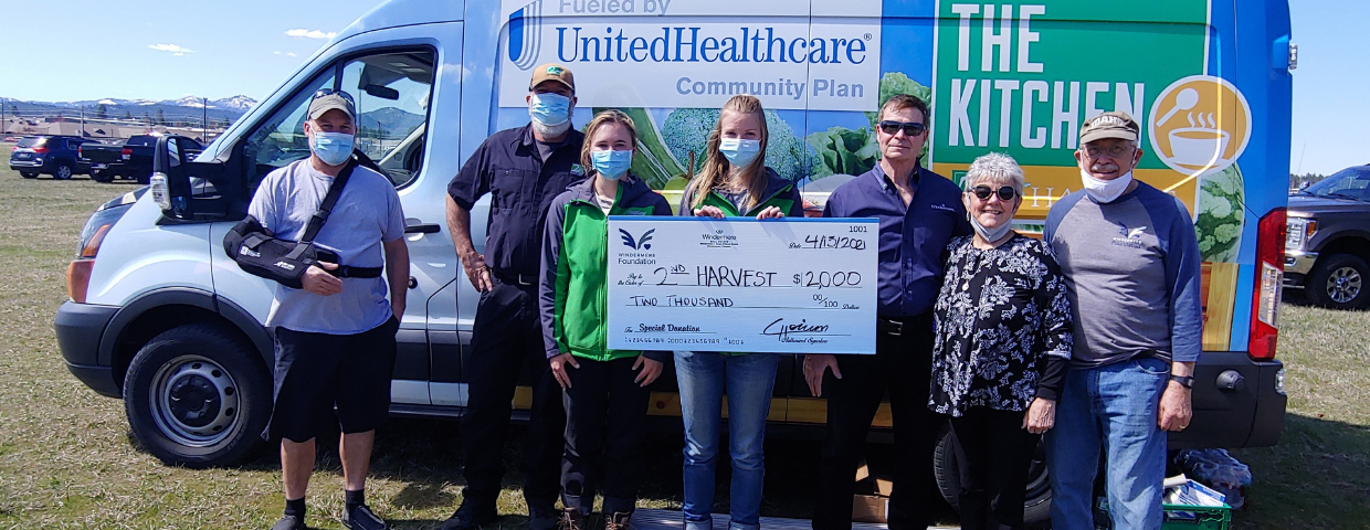 A group of people hold a $2,000 check in front of a van.